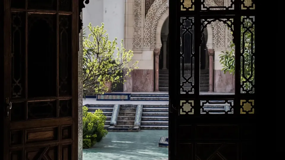 Porte en bois sculpté ouverte sur le patio de la Grande Mosquée de Paris, ses arcades et son bassin
